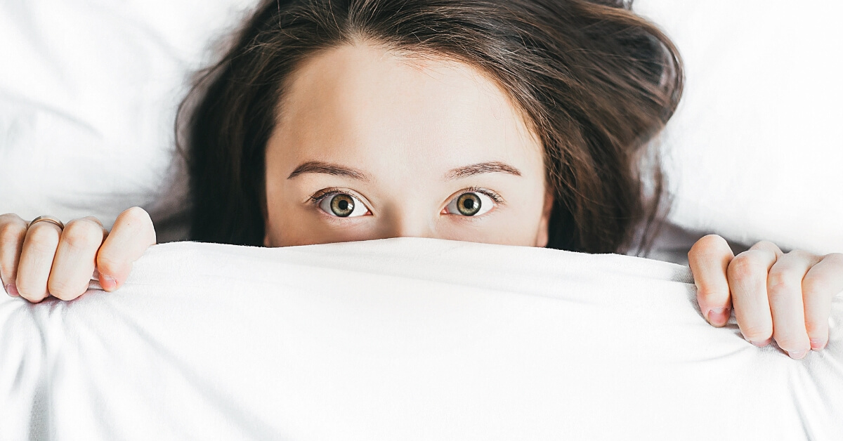woman peeking out from under bed covers