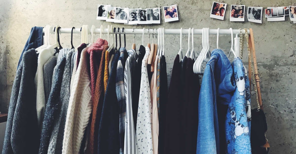 A rack of various sweaters and jumper hanging on coat hangers against a wall