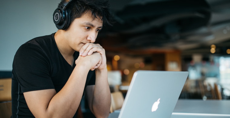 Photo of a young man with headphones on working on a laptop